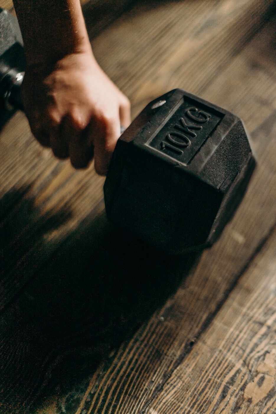 Una mano toma una mancuerna de 10 kilos en el suelo de madera de un gimnasio.